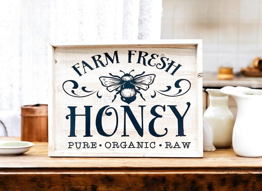 Farm Fresh Honey framed reclaimed wood sign with navy bee graphic and chalk paste lettering in distressed whitewash frame on rustic wood breakfast table with honey jar berries and biscuits