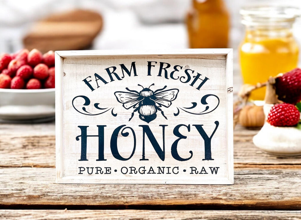 Farm Fresh Honey framed reclaimed wood sign with navy bee graphic and chalk paste lettering in distressed whitewash frame on rustic wood surface with honey jars blueberries and raspberries
