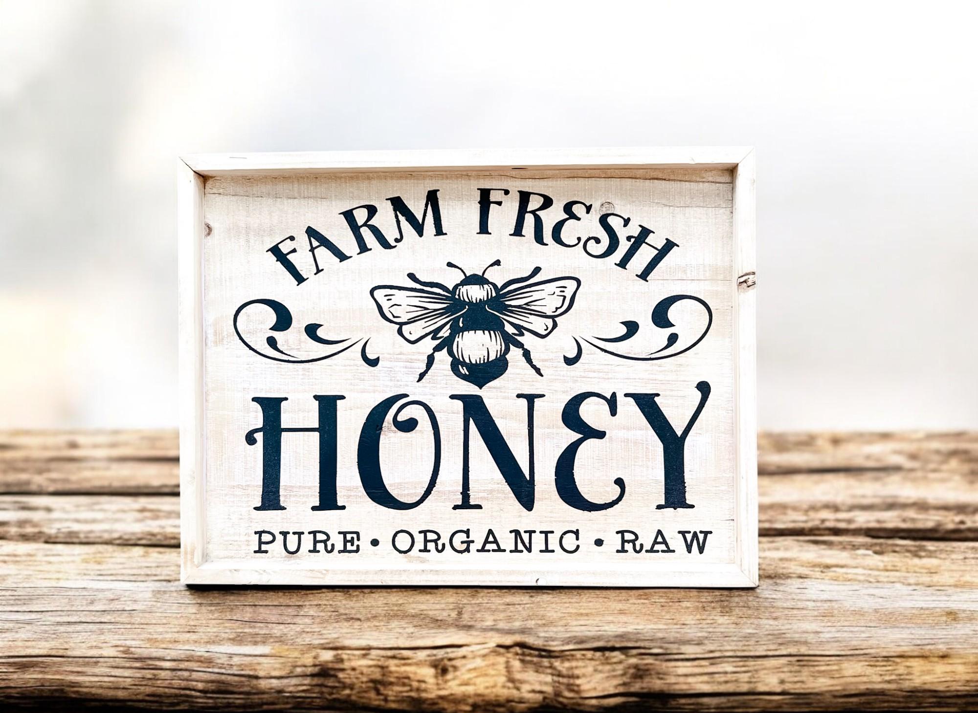 Farm Fresh Honey framed reclaimed wood sign with navy bee graphic and chalk paste lettering in distressed whitewash frame on rustic wood surface with honey jars and raspberries wide shot
