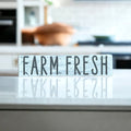 Farm Fresh distressed white wood sign with dark grey lettering on light wood kitchen counter with modern kitchen background