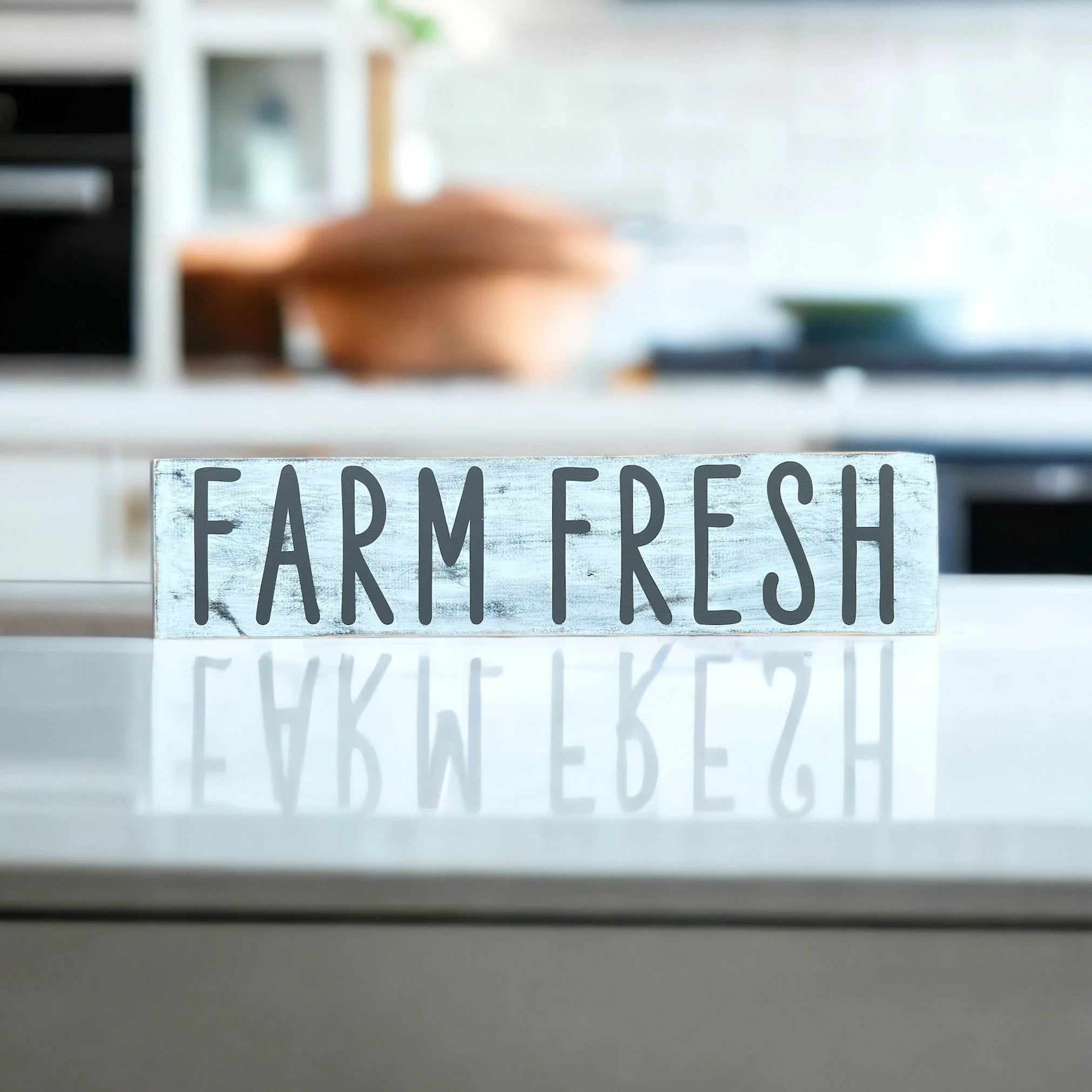 Farm Fresh distressed white wood sign with dark grey lettering on light wood kitchen counter with modern kitchen background