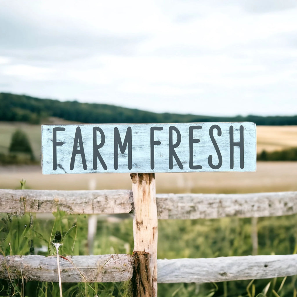 Farm Fresh distressed white wood sign with dark grey lettering flat lay on rustic wood plank surface
