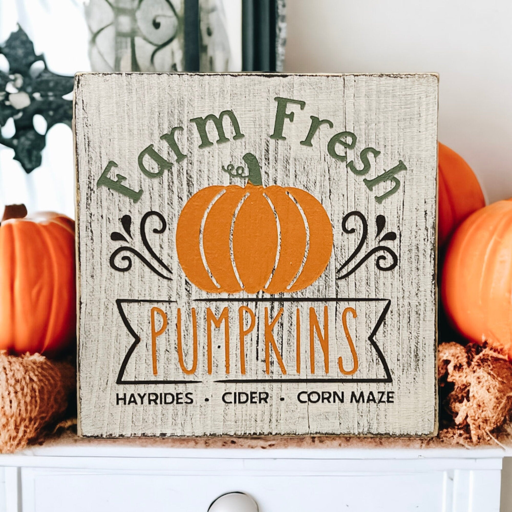 Farm Fresh Pumpkins wood block sign on rustic wood surface with autumn foliage background