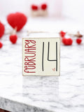 February 14 wood block sign with red roses and fairy lights on rustic wood table
