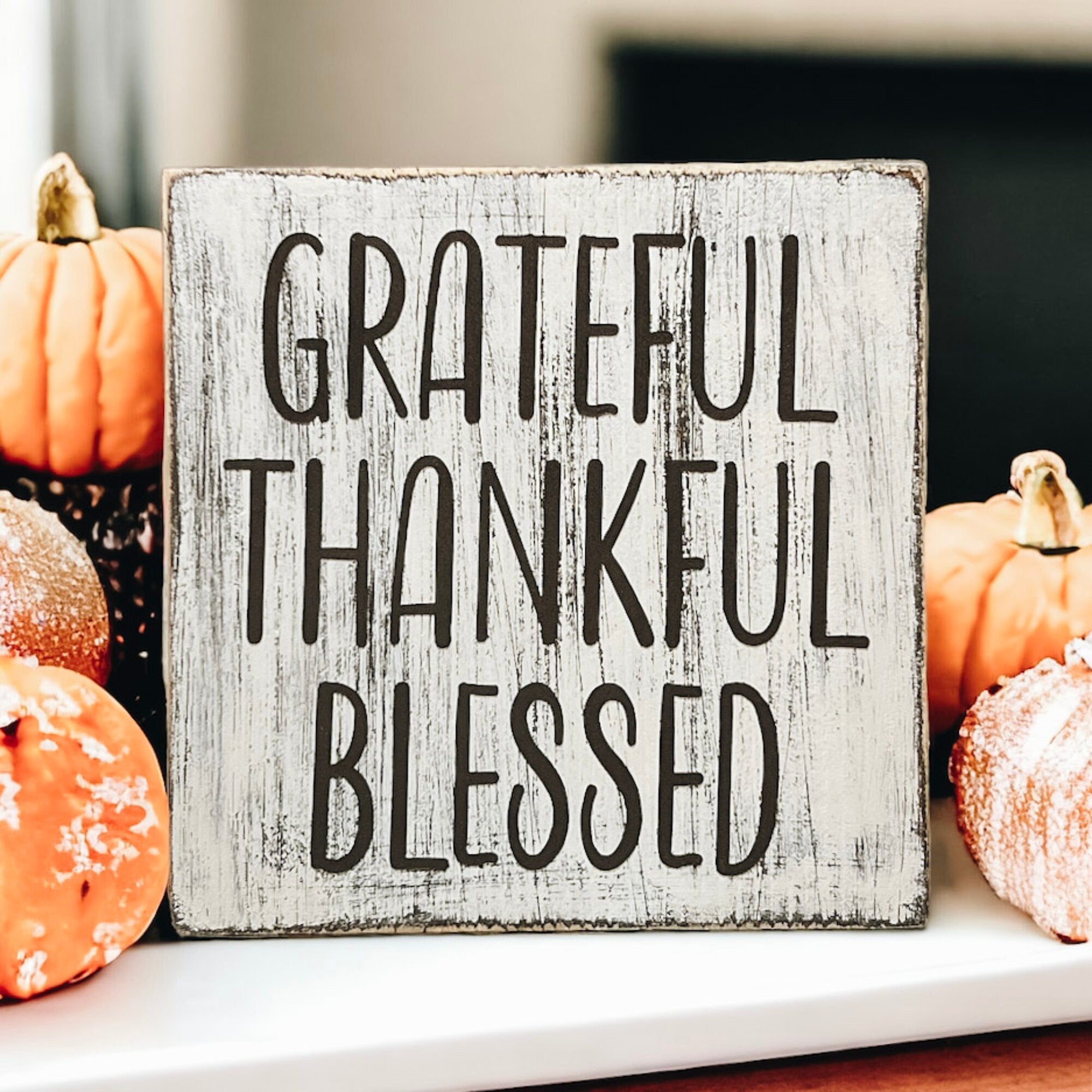 Grateful Thankful Blessed distressed white wood block sign on white mantel with orange pumpkins and pine cone bowl