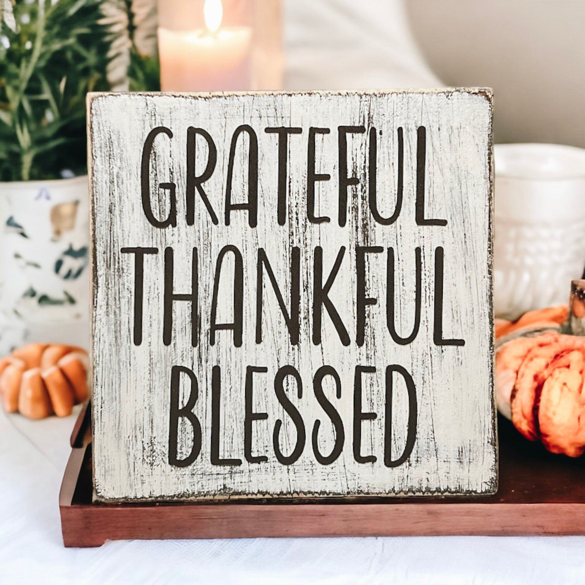 Grateful Thankful Blessed distressed white wood block sign on wood surface with white candles and mini pumpkins with bokeh lights