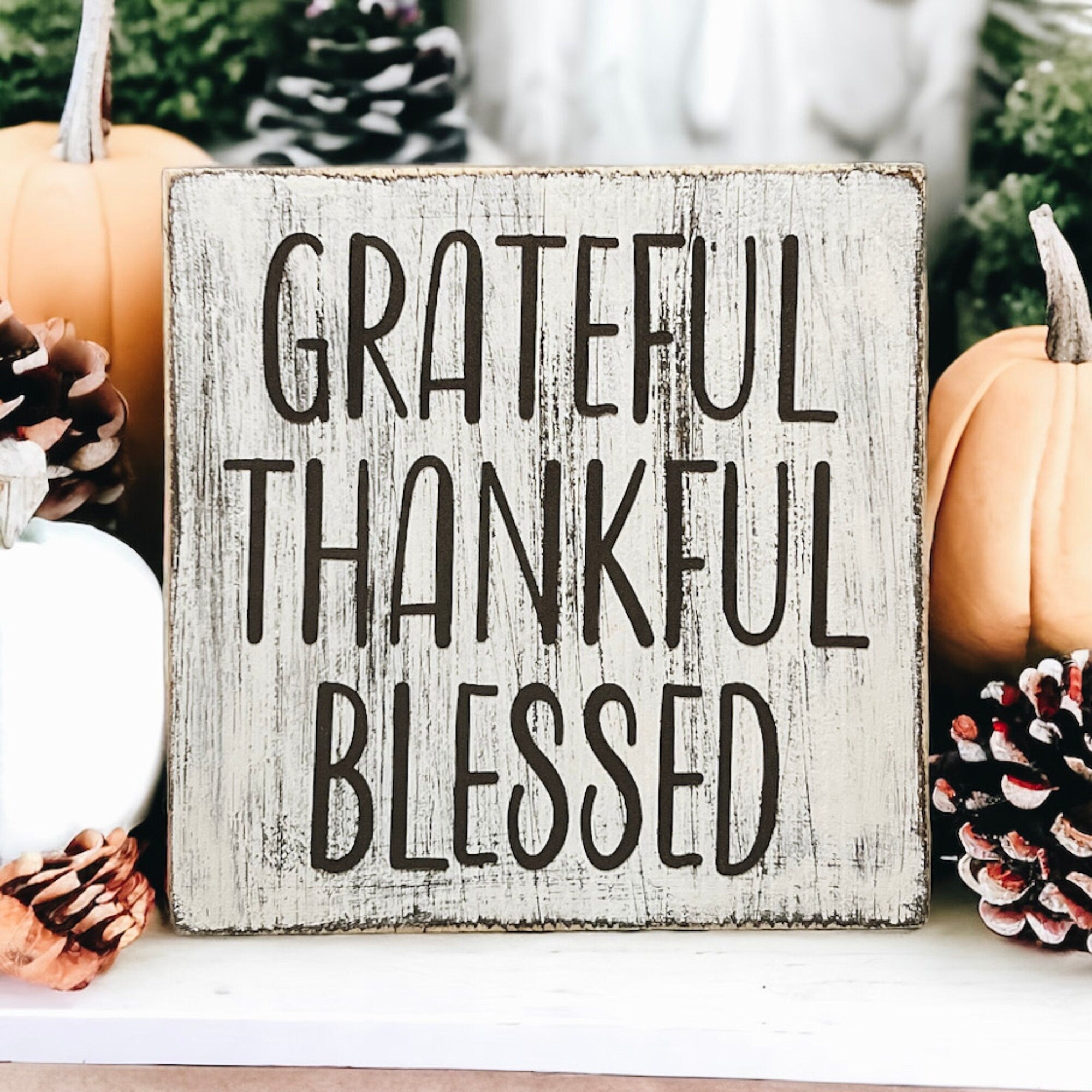 Grateful Thankful Blessed distressed white wood block sign on white cake stand with orange pumpkins and red berry stems