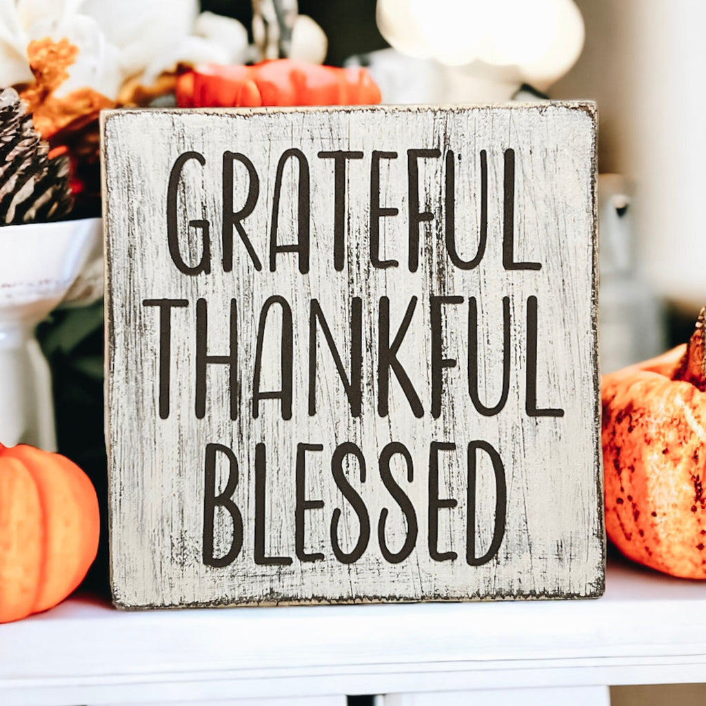 Grateful Thankful Blessed distressed white wood block sign on wood tray with candle and pumpkins on white table