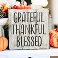Grateful Thankful Blessed distressed white wood block sign on wood tray with candle and pumpkins on white table