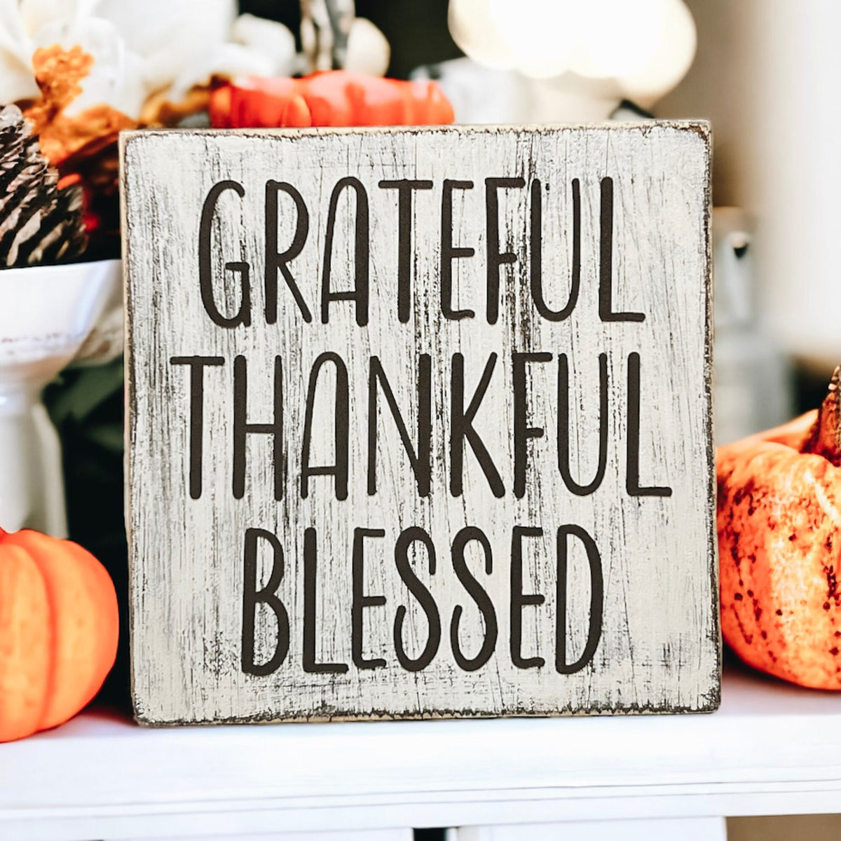 Grateful Thankful Blessed distressed white wood block sign on wood tray with candle and pumpkins on white table