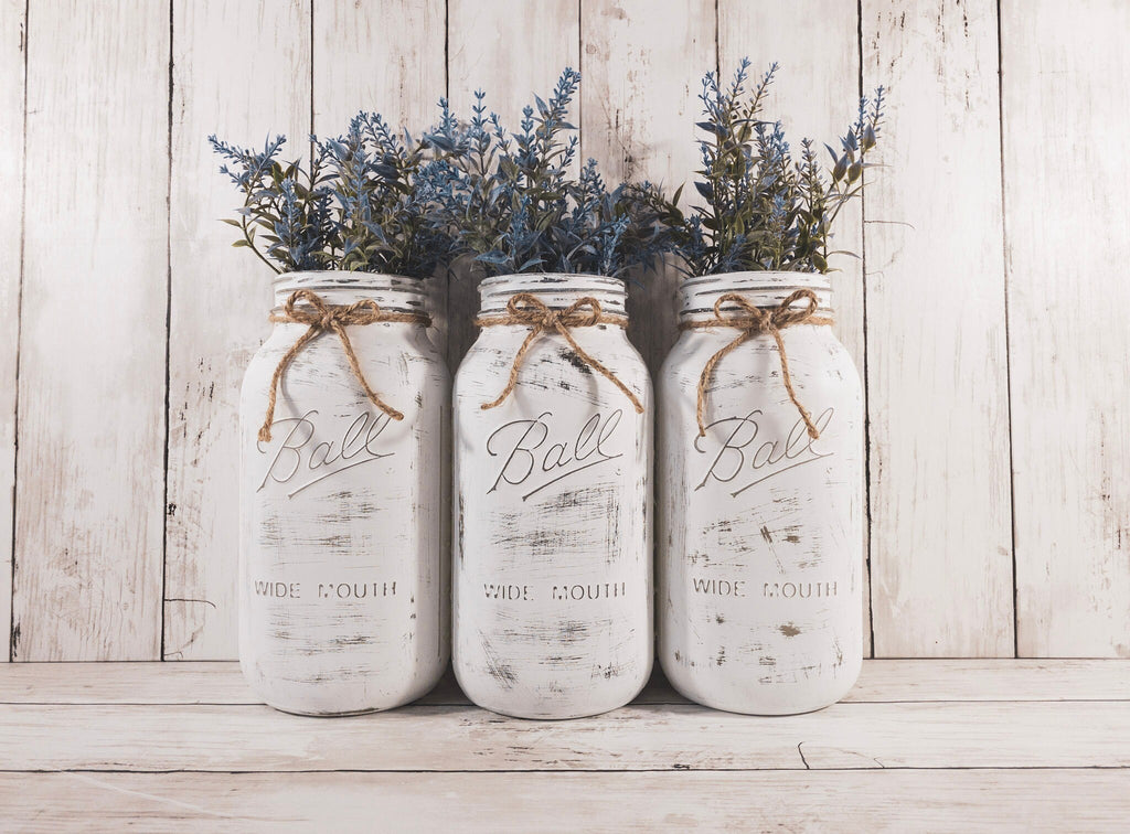 Set of 3 distressed white Ball mason jars with jute twine bows on white wood surface front view