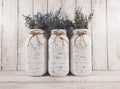 Set of 3 distressed white Ball mason jars with jute twine bows on white wood surface front view