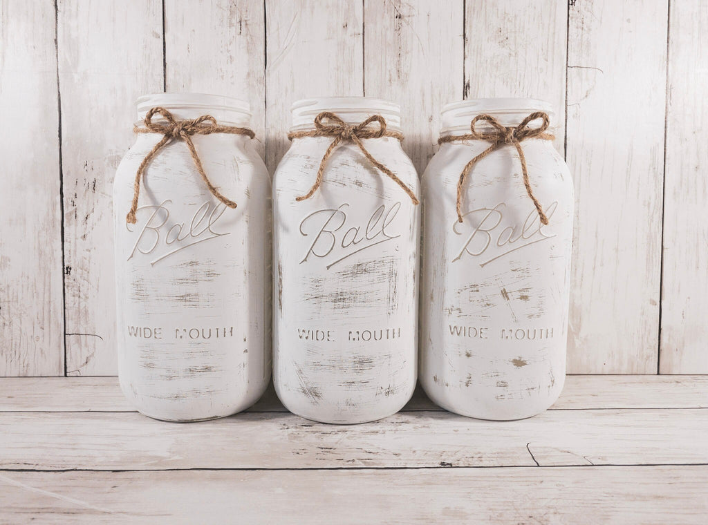 Set of 3 distressed white Ball mason jars with jute twine bows styled on white wood surface