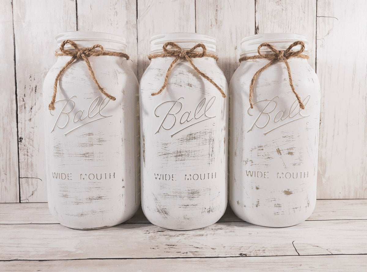 Set of 3 distressed white Ball mason jars with jute twine bows close up on white wood surface