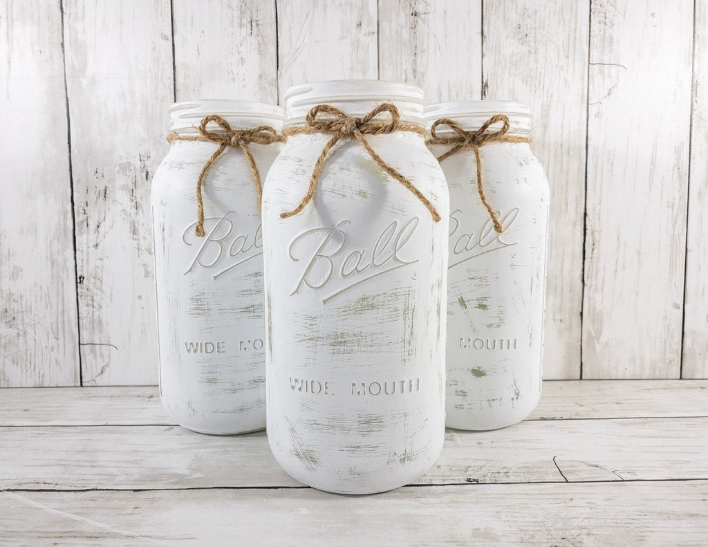 Set of 3 distressed white Ball mason jars with jute twine bows angled view on white wood surface