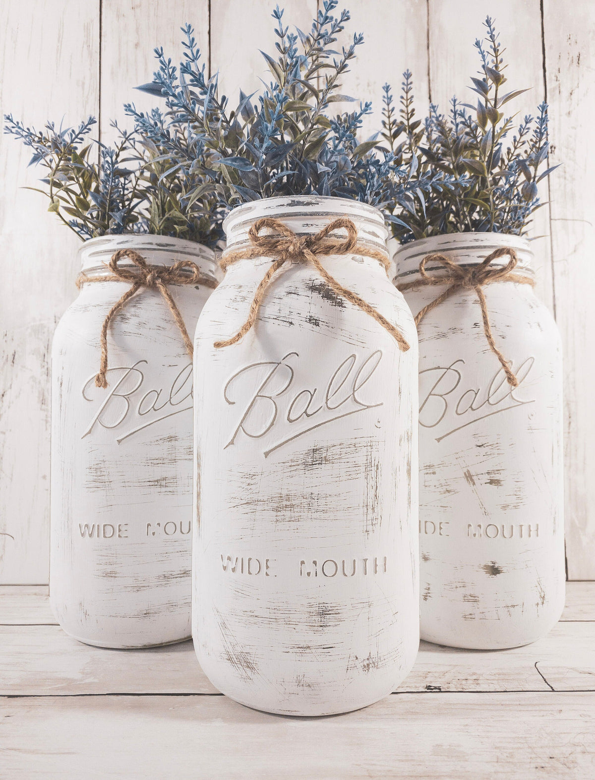 Set of 3 distressed white Ball mason jars with jute twine bows product shot on white wood surface
