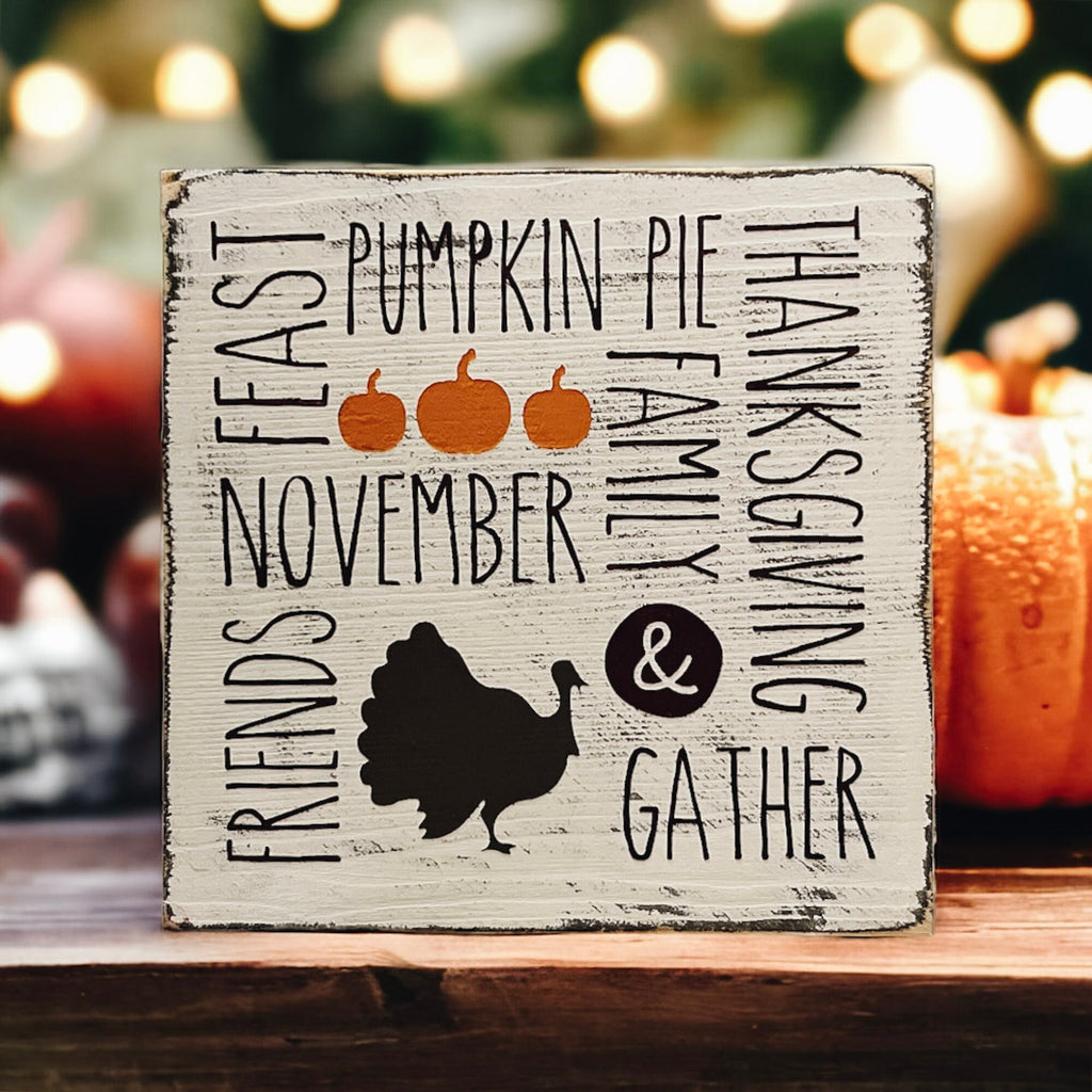 Thanksgiving farmhouse word collage wood block sign with turkey silhouette on rustic wood surface with white vase and bokeh lights