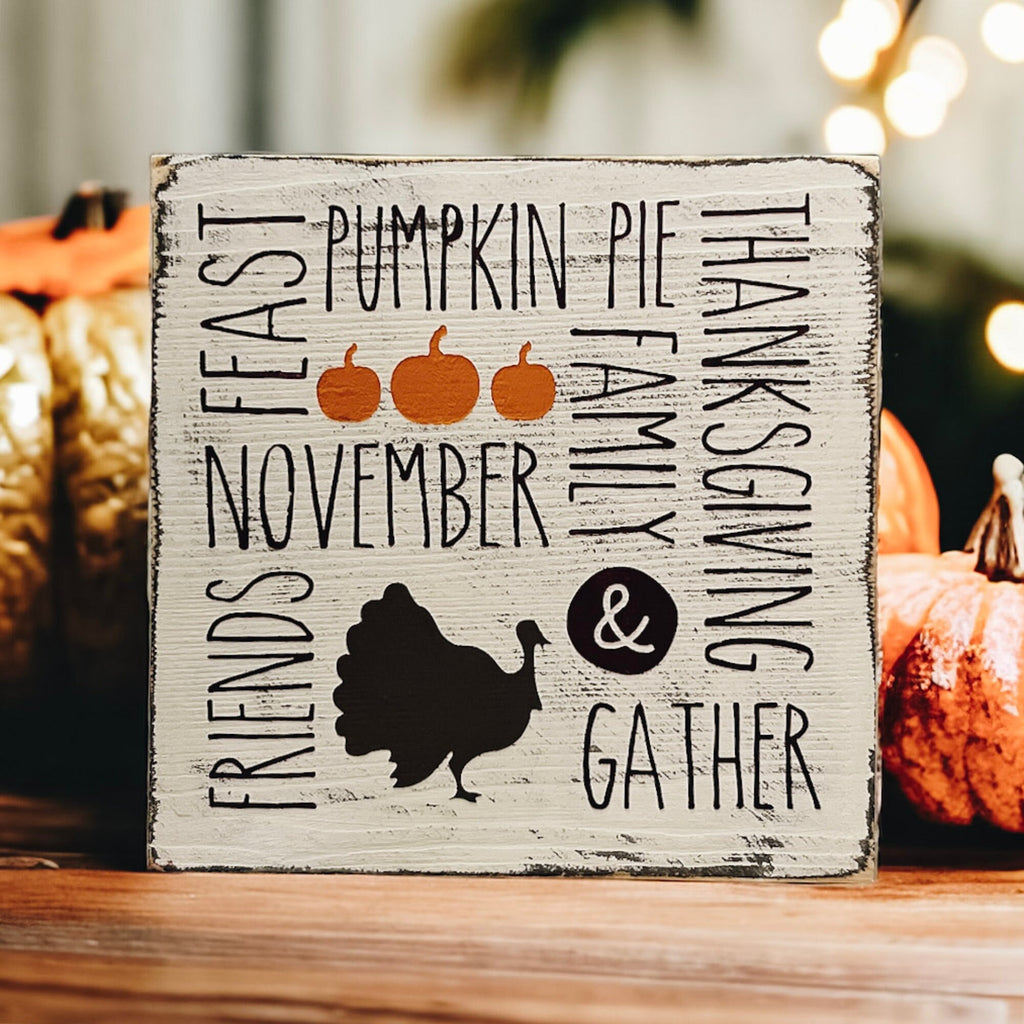 Thanksgiving farmhouse word collage wood block sign with turkey silhouette on rustic wood surface with candles and warm holiday lights