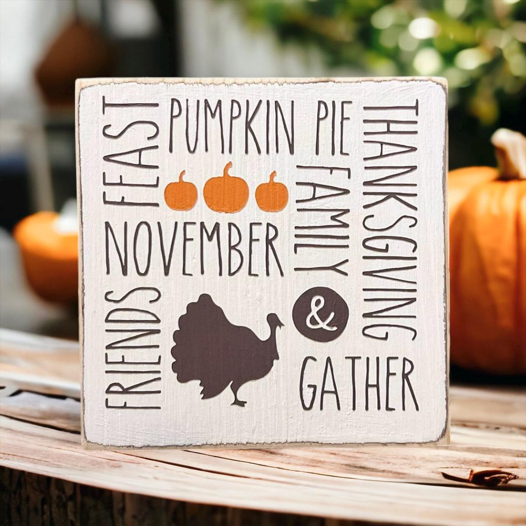 Thanksgiving farmhouse word collage wood block sign with turkey silhouette on rustic wood surface with pumpkins and warm bokeh lights