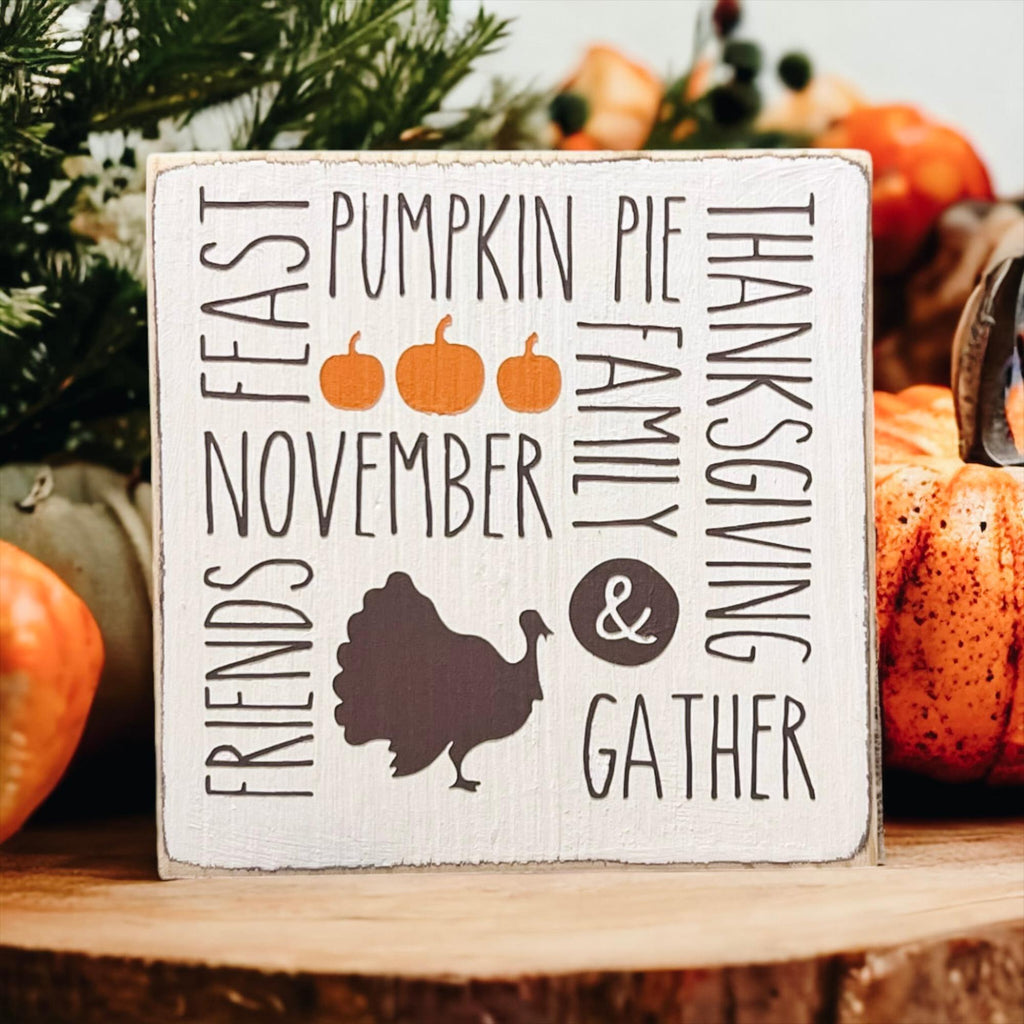 Thanksgiving farmhouse word collage wood block sign with turkey silhouette and orange pumpkins on rustic wood surface with bokeh lights