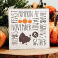Thanksgiving farmhouse word collage wood block sign with turkey silhouette and orange pumpkins on rustic wood surface with bokeh lights