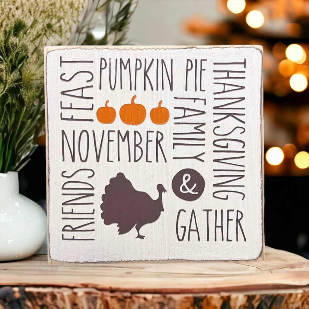 Thanksgiving farmhouse word collage wood block sign with turkey silhouette on rustic wood surface with orange pumpkins close up product shot
