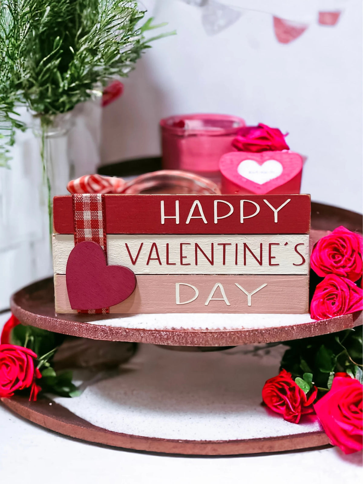 Happy Valentine's Day wood book stack with pine cones and red heart ornaments on white wood table