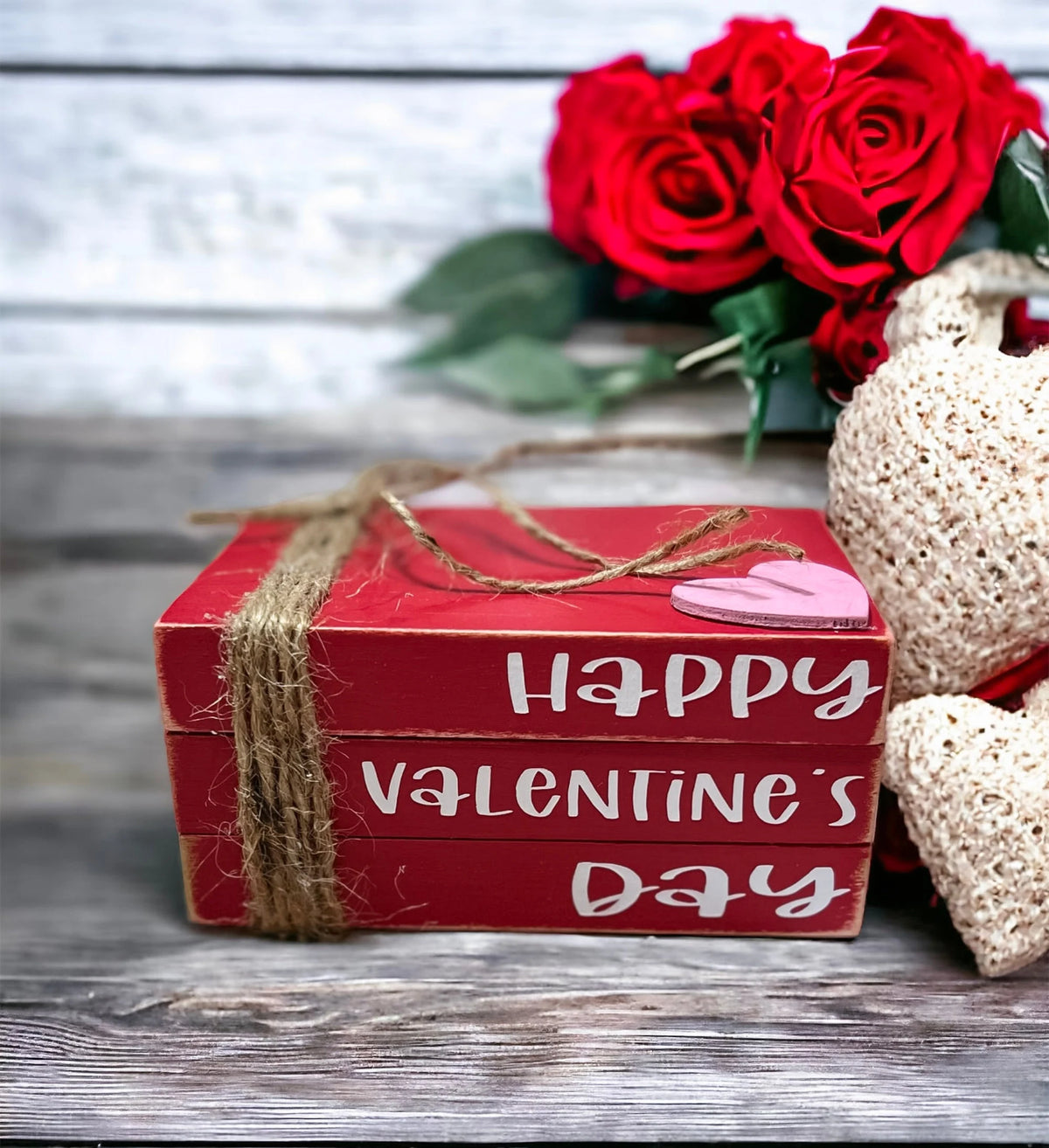 Happy Valentine's Day red wood book stack with jute twine and pink heart on rustic wood surface with Christmas lights and red heart ornaments