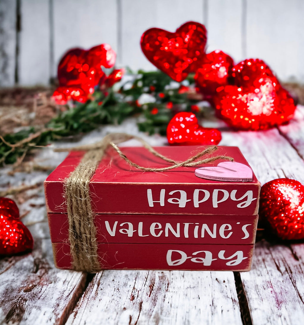 Happy Valentine's Day red wood book stack with jute twine and pink heart on rustic wood surface styled view