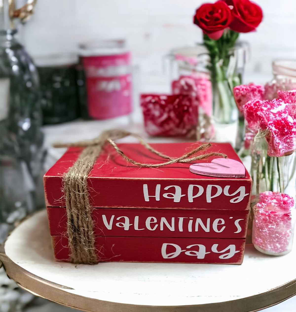 Happy Valentine's Day red wood book stack with jute twine and pink heart on rustic wood surface with red roses close up
