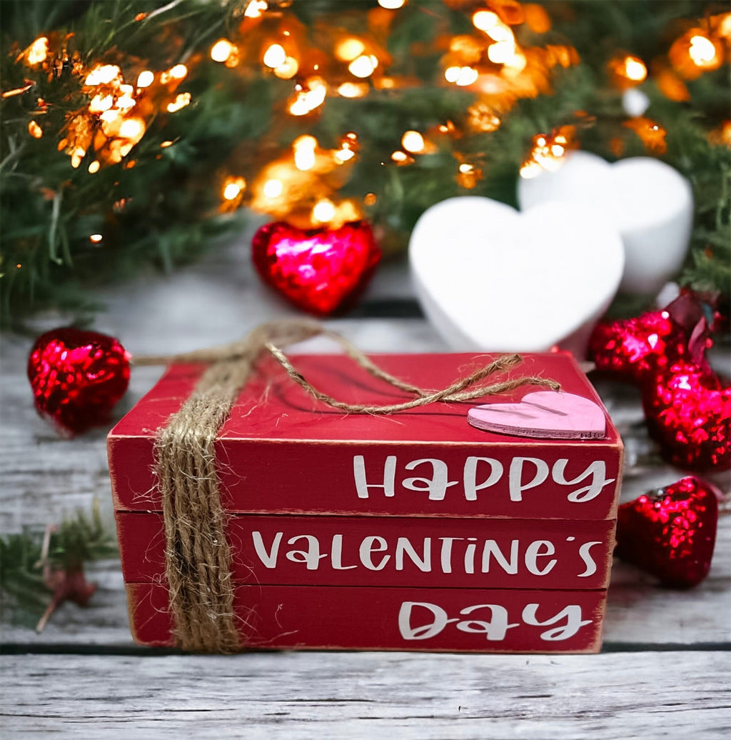 Happy Valentine's Day red wood book stack with jute twine and pink heart on rustic wood surface with glitter red hearts and bokeh lights