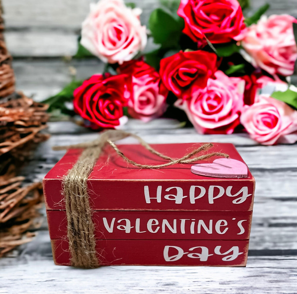 Happy Valentine's Day red wood book stack with jute twine and pink heart on rustic wood surface with red rose and felt heart