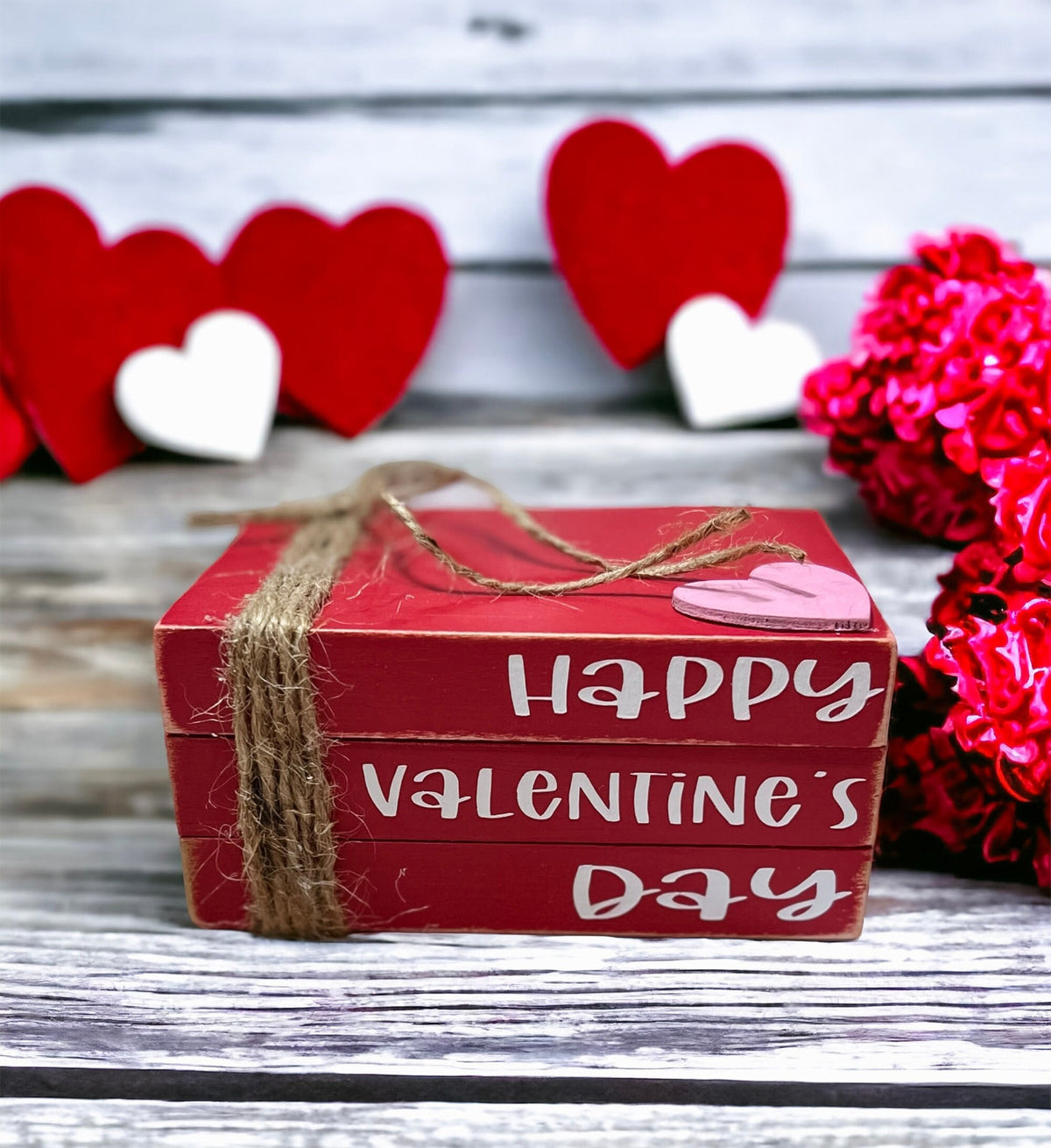 Happy Valentine's Day red wood book stack with jute twine and pink heart on rustic wood surface with pine cones and bokeh lights
