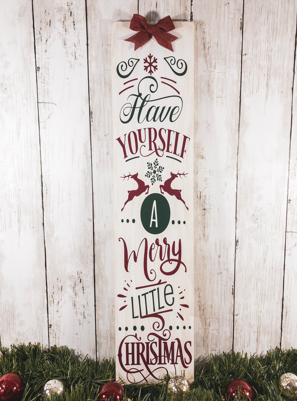Have Yourself a Merry Little Christmas rustic wood porch leaner sign with burlap bow on white wood wall beside glitter Christmas trees wide view