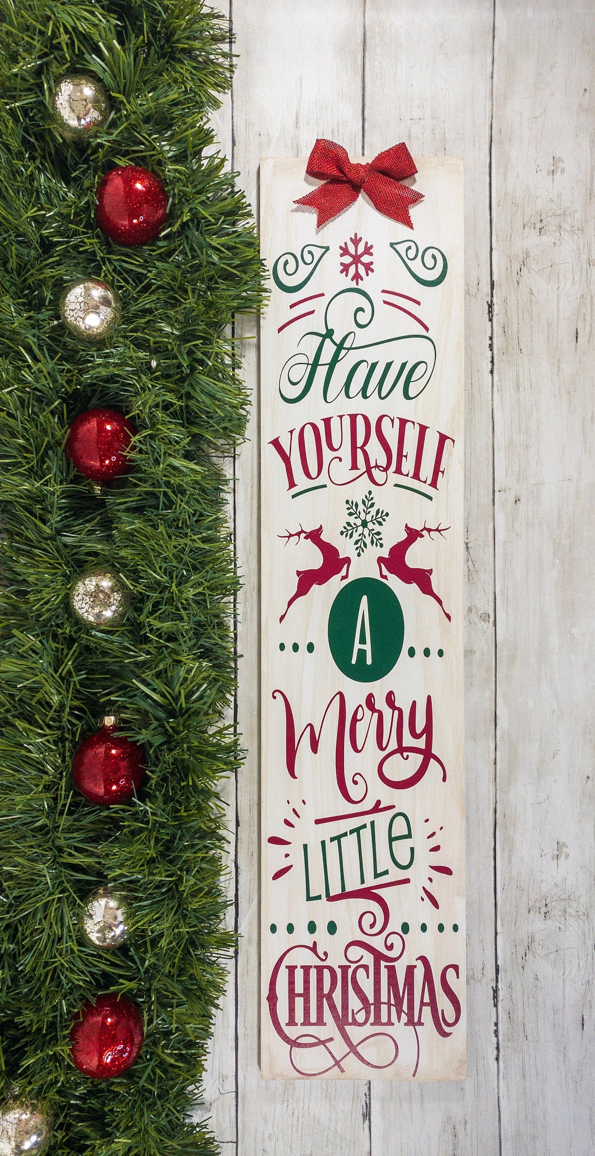 Have Yourself a Merry Little Christmas rustic wood porch leaner sign with burlap bow on white wood wall beside glitter Christmas trees close up
