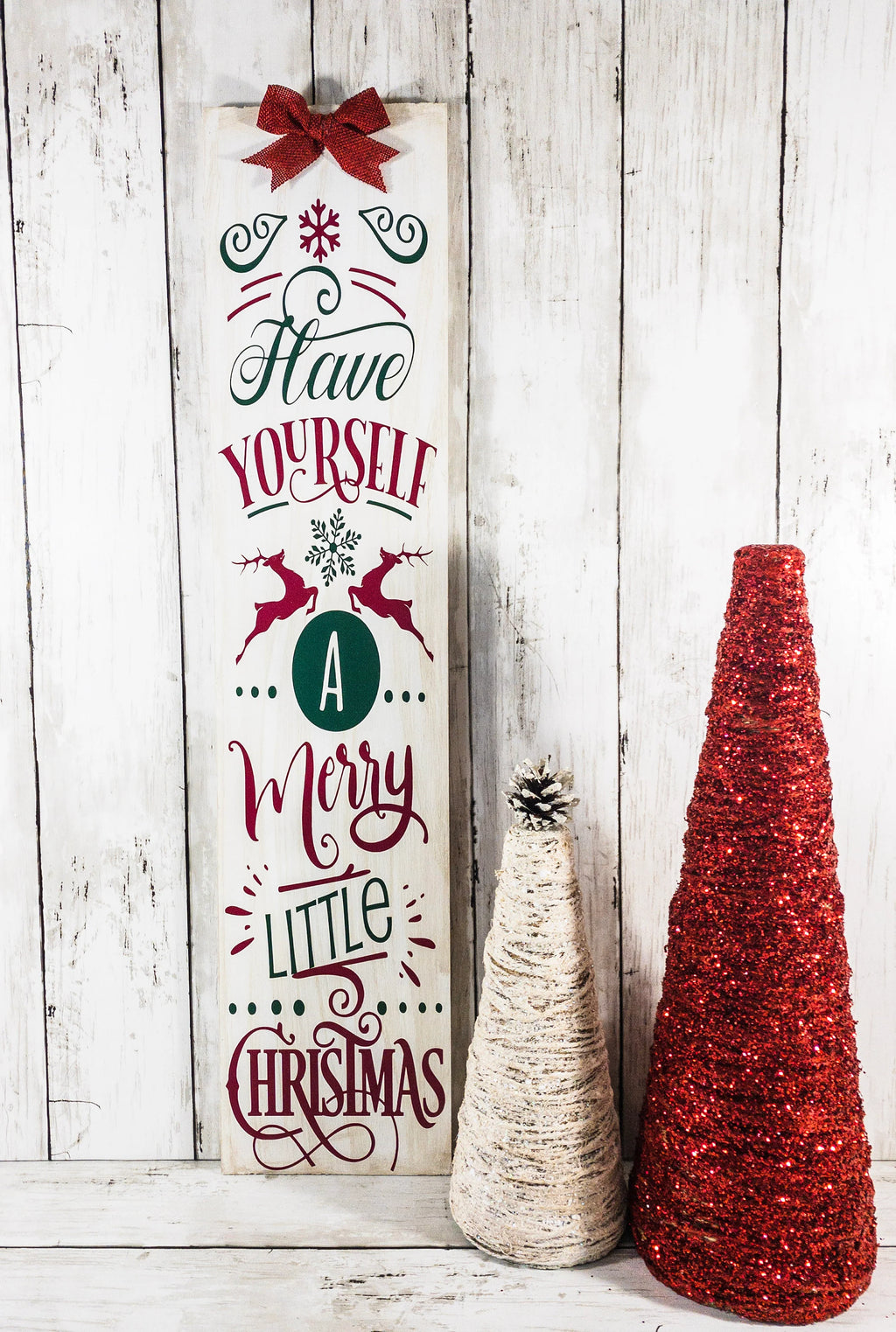 Have Yourself a Merry Little Christmas rustic wood porch leaner sign with burlap bow on white wood wall beside glitter Christmas trees and ornaments