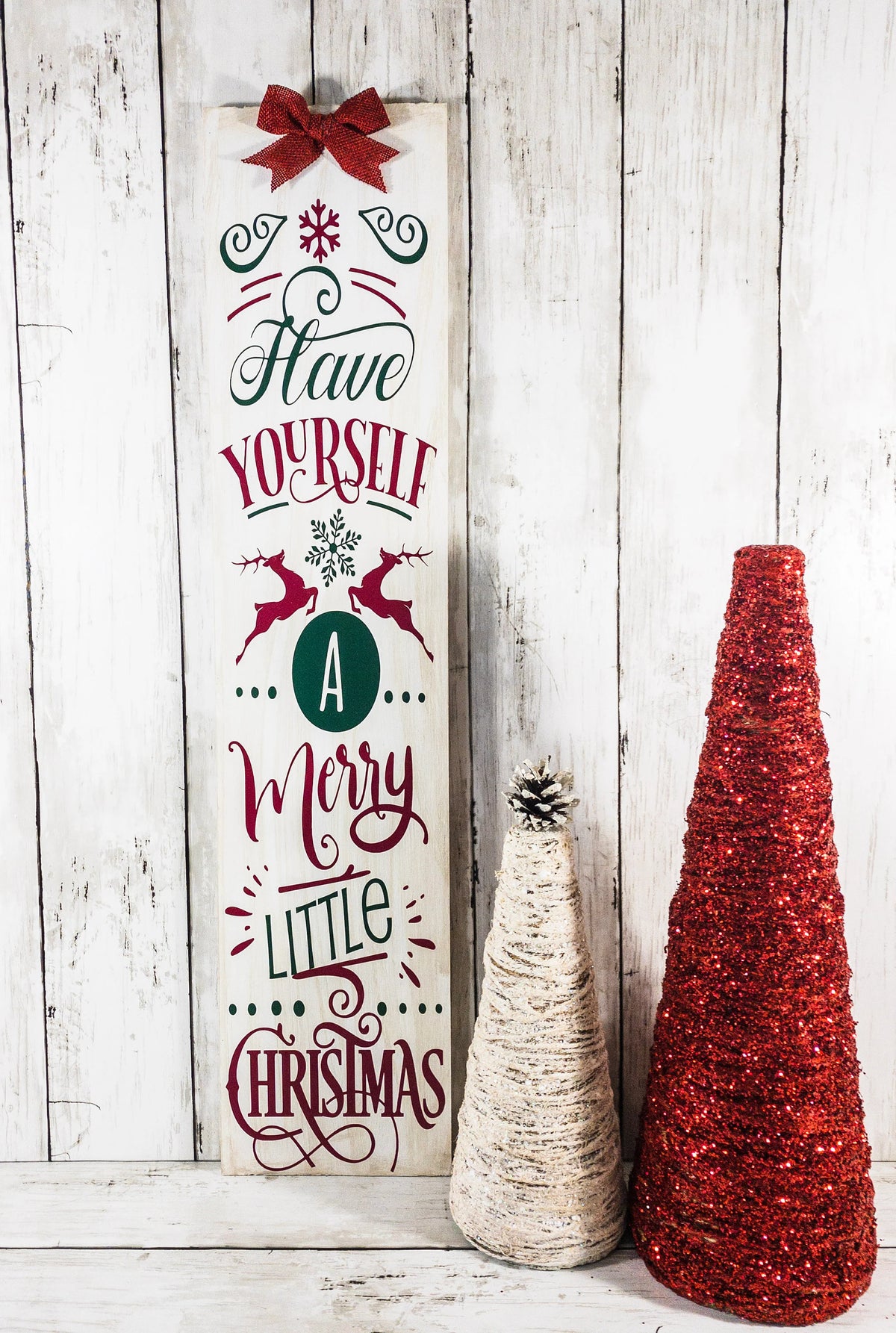 Have Yourself a Merry Little Christmas rustic wood porch leaner sign with burlap bow on white wood wall beside glitter Christmas trees and ornaments