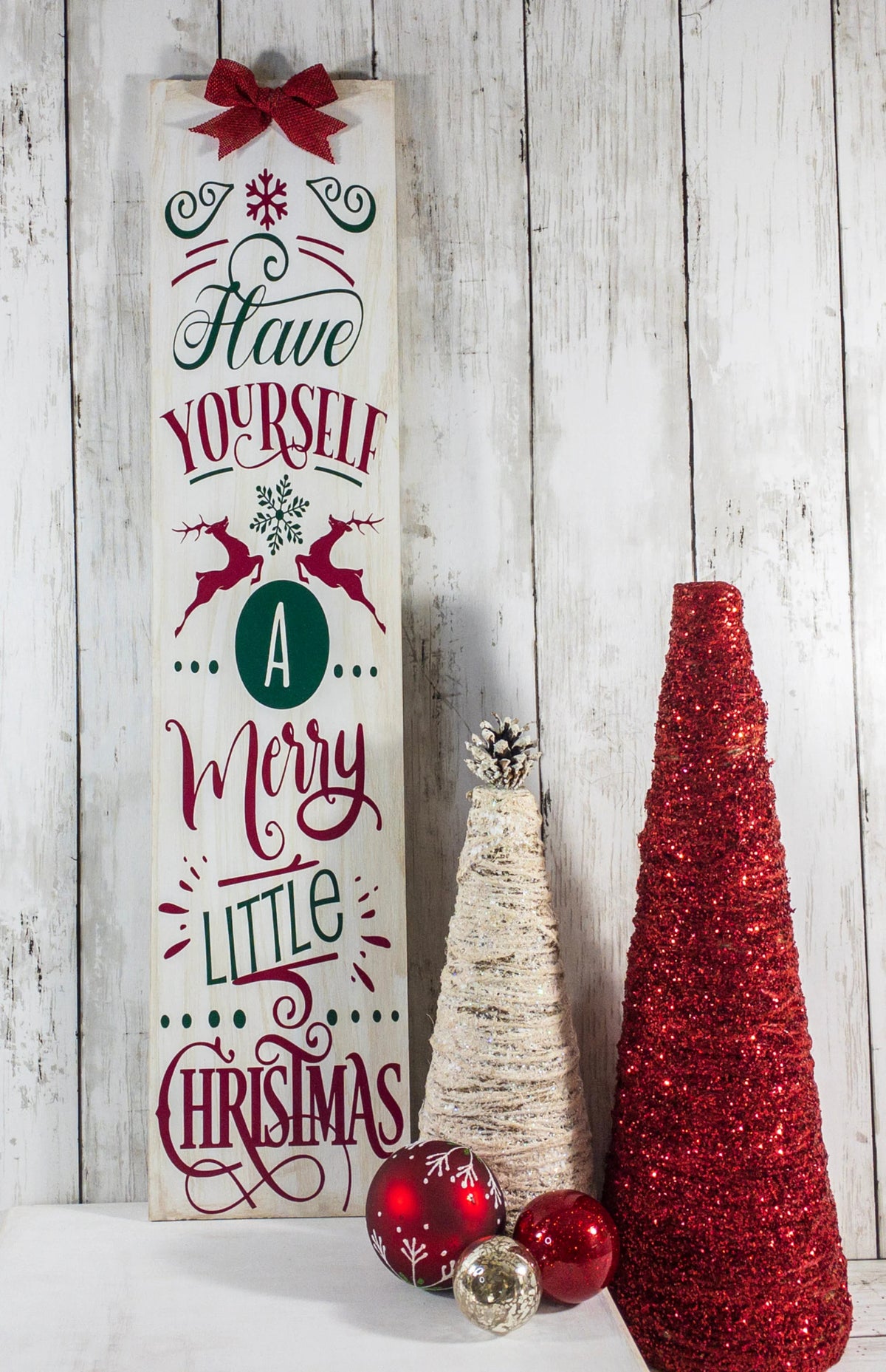 Have Yourself a Merry Little Christmas rustic wood porch leaner sign with burlap bow leaning against white door beside boxwood topiary