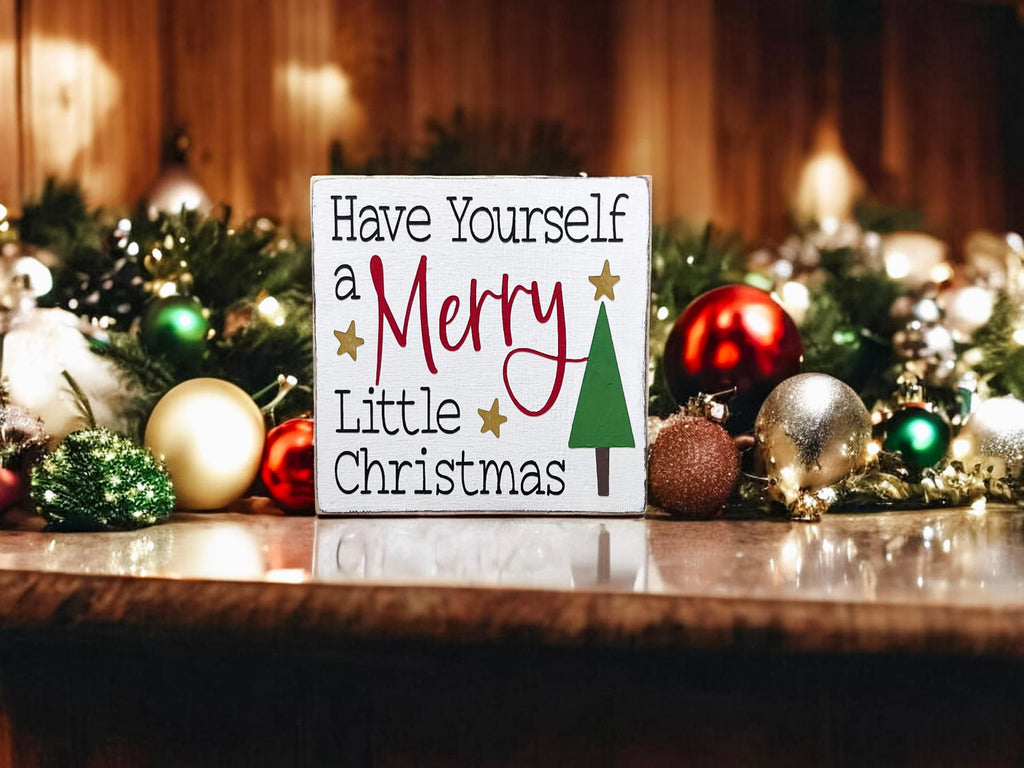 Have Yourself a Merry Little Christmas white wood block sign on kitchen counter with red and gold ornaments and pine garland