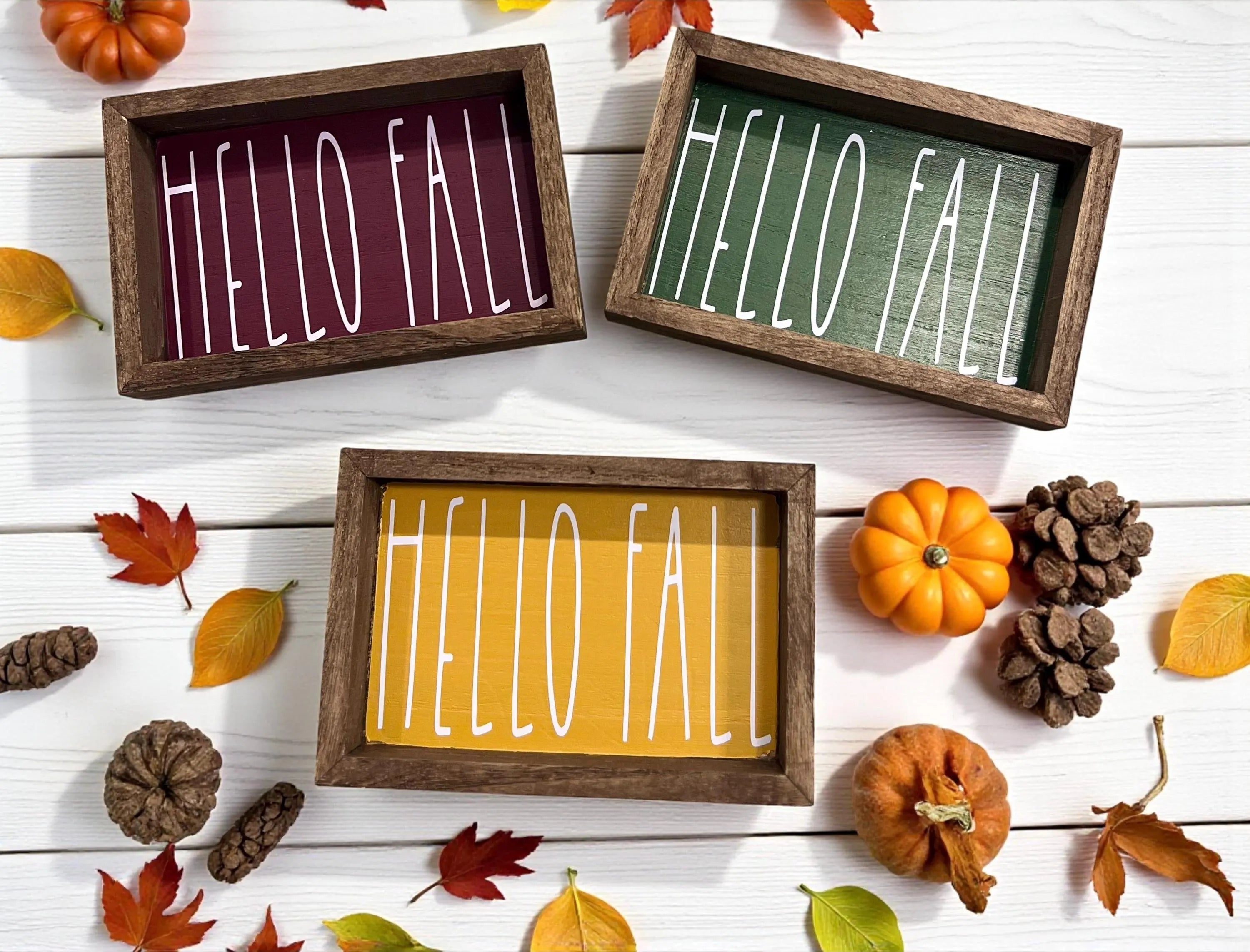 Hello Fall framed wood sign in all three colors cranberry golden yellow and pine green on white wood surface with apples and pumpkins wide view
