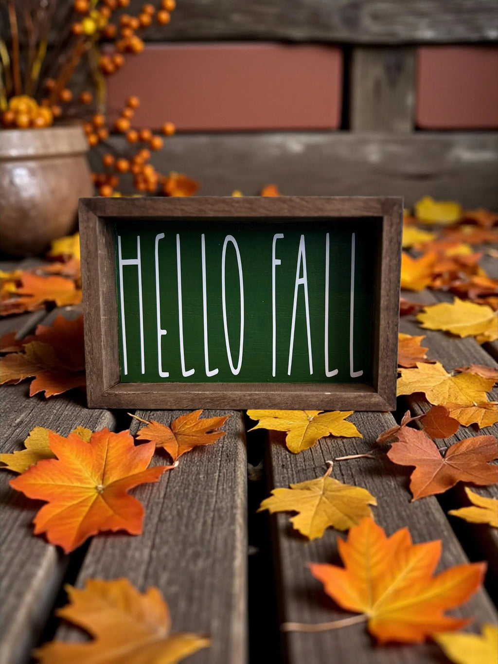 Hello Fall pine green framed wood sign on rustic wood surface with orange berry stems and fall leaves