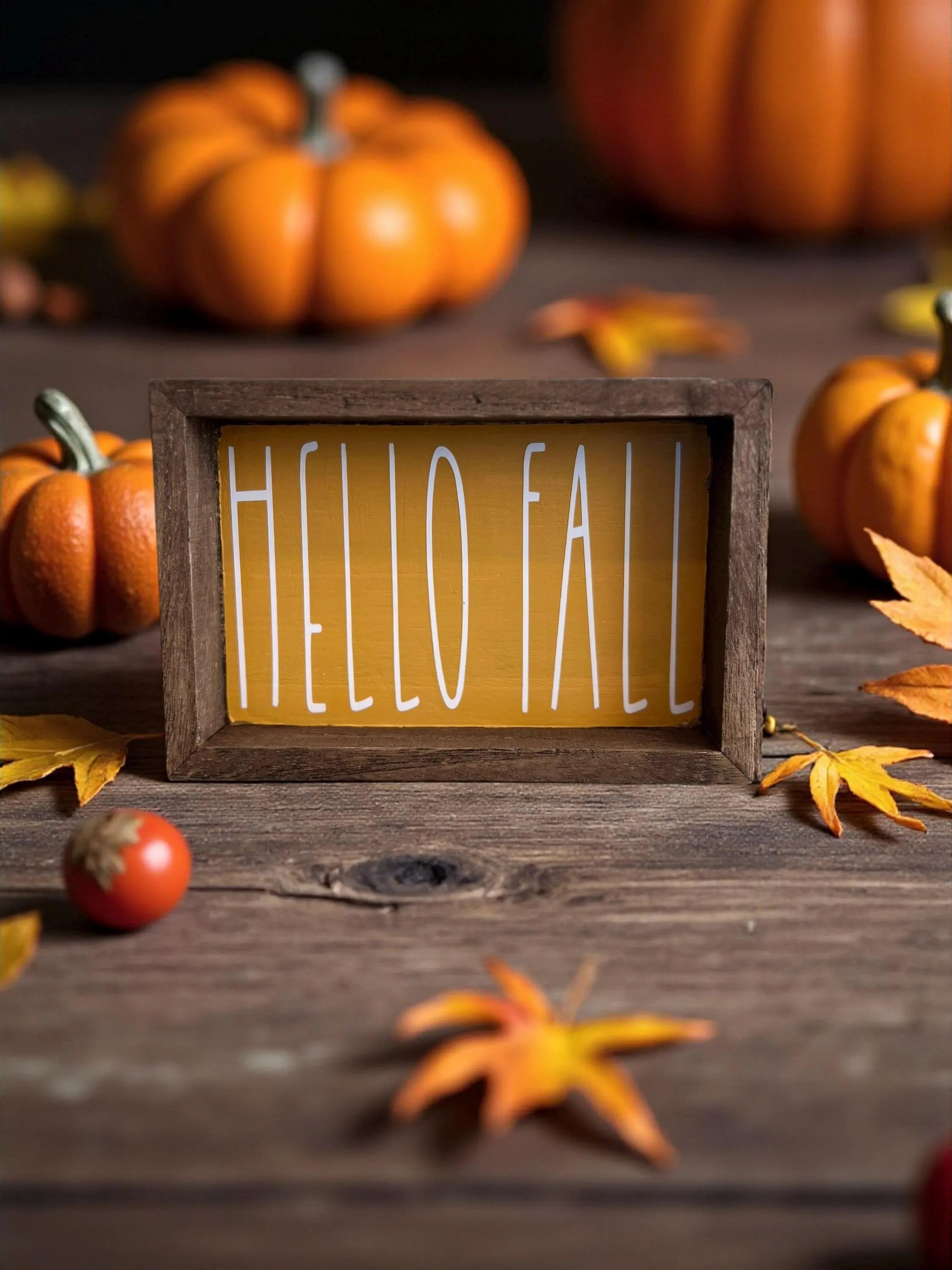 Hello Fall golden yellow framed wood sign on rustic wood surface with orange pumpkins and fall leaves