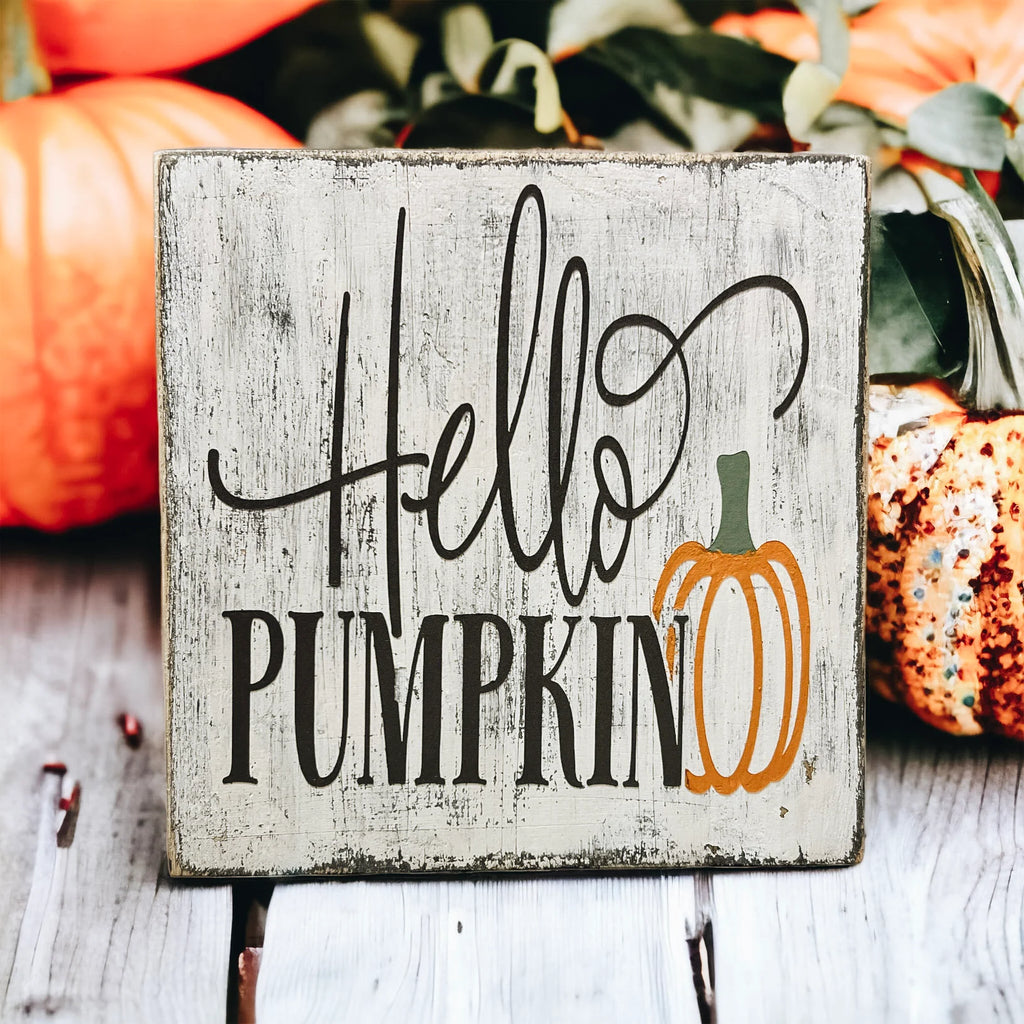 Hello Pumpkin wood block sign with black script and serif lettering and orange pumpkin graphic on distressed white pine on white tiered tray with orange pumpkins and fall leaves wide shot