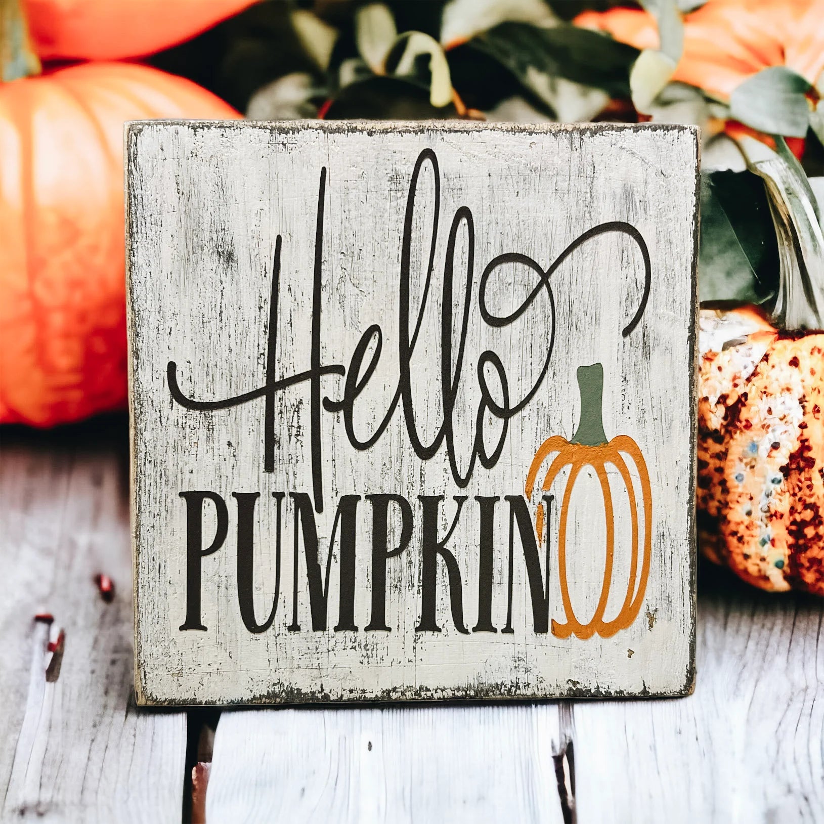 Hello Pumpkin wood block sign with black script and serif lettering and orange pumpkin graphic on distressed white pine on white tiered tray with orange pumpkins and fall leaves wide shot