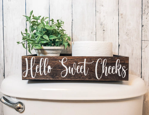 Hello Sweet Cheeks dark stained farmhouse toilet paper box on toilet tank with plant and toilet paper roll wide view