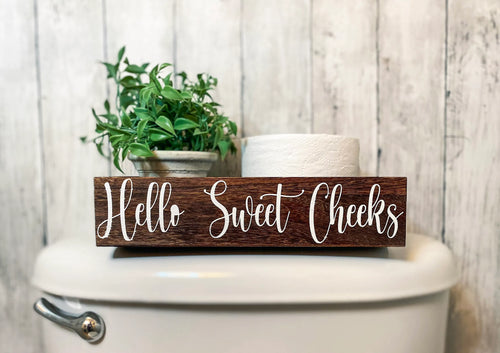 Hello Sweet Cheeks dark stained farmhouse toilet paper box on toilet tank with plant and toilet paper roll front view