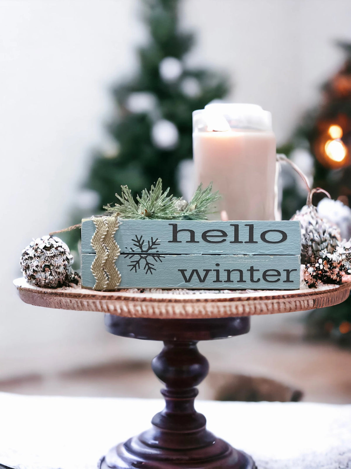 Hello Winter dusty blue wood book stack with snowflake and burlap ribbon close up on wood surface with frosted pine sprig
