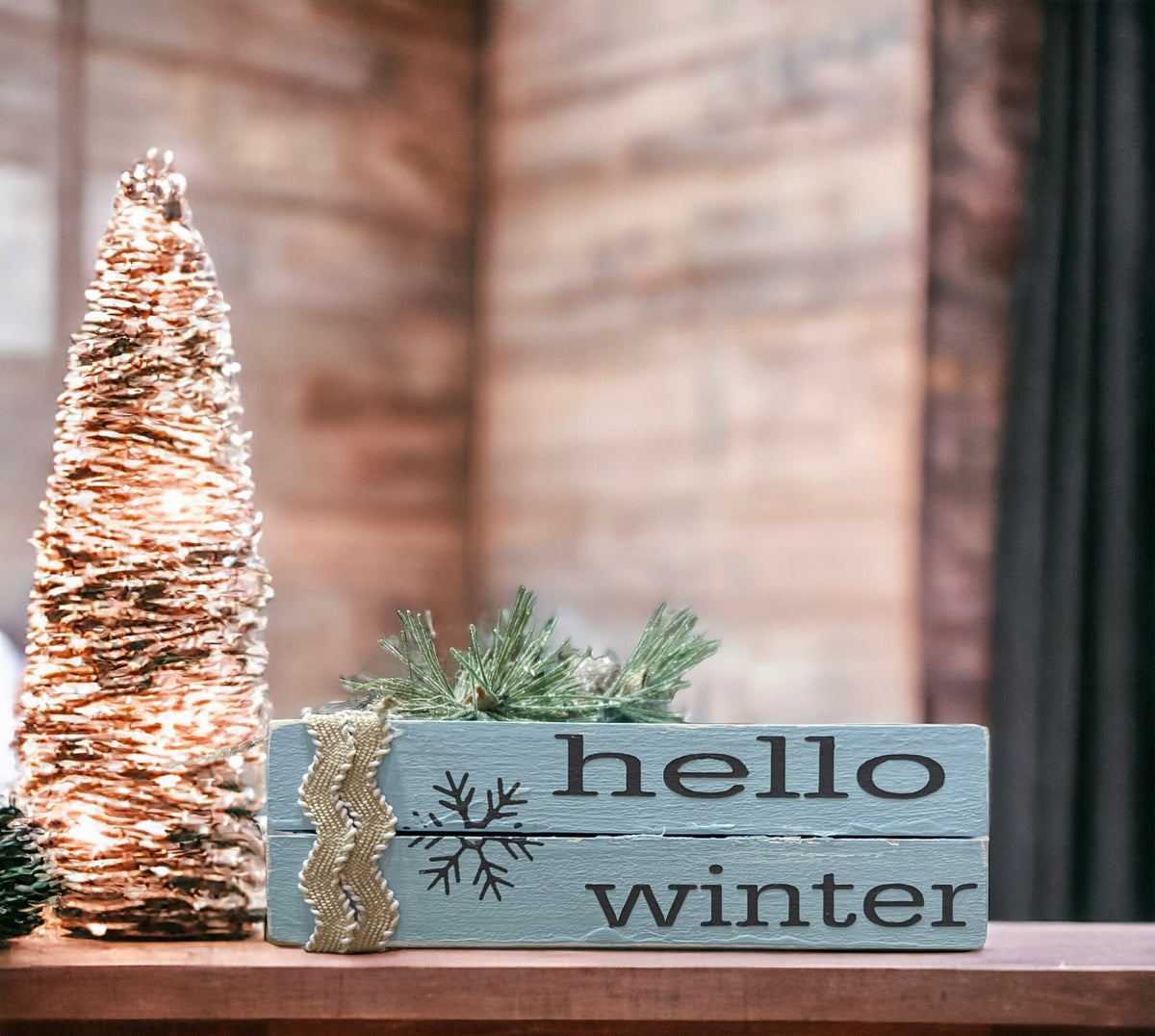 Hello Winter dusty blue wood book stack with snowflake and burlap ribbon on dark tiered tray with pine cone and red berries