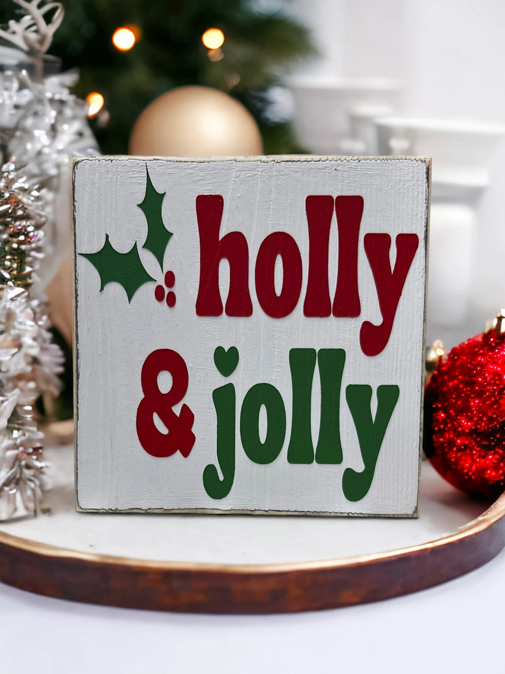Holly & Jolly wood sign with pine cones and candles on white wood surface