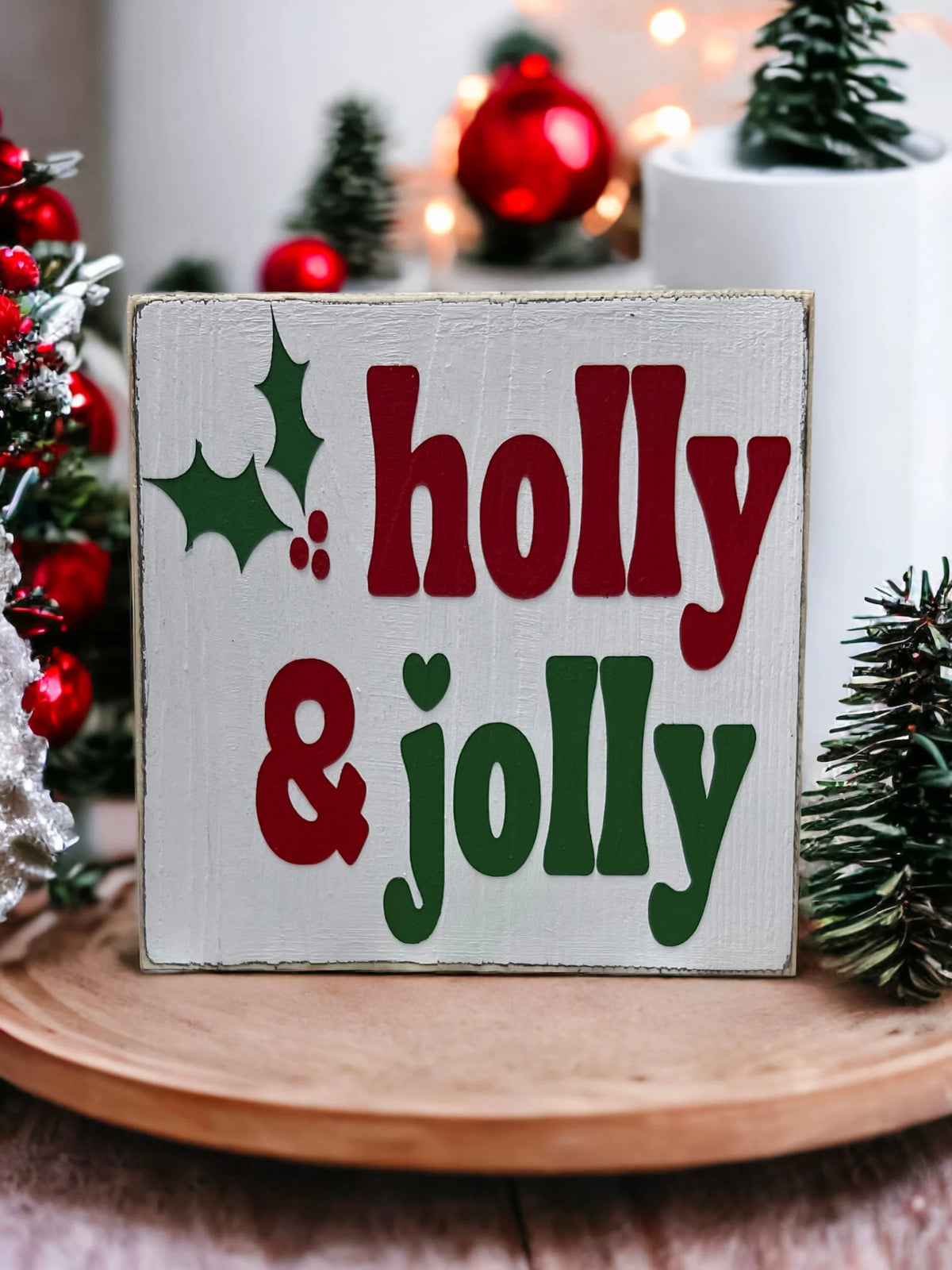 Holly & Jolly wood sign with pine cones and red candle on white wood